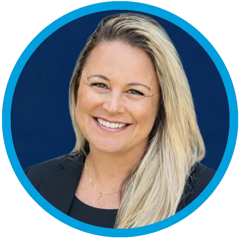 Portrait of a smiling woman with long brown hair, wearing a coral blazer over a white top, set against a dark blue background with a bright blue circular border.