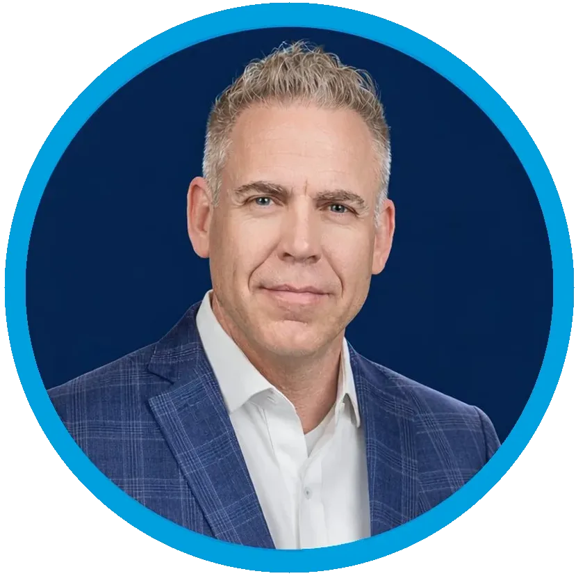 A man with short gray hair wearing a white shirt and blue plaid suit jacket, shown in a circular frame with a blue border on a plain white background.